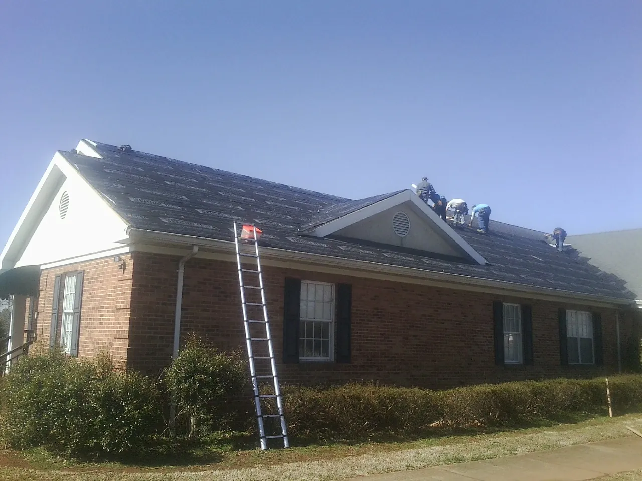 Crew tearing shingles off a brick ranch roof with a ladder set — Emergency Roof Repair work by our crew in Boylston