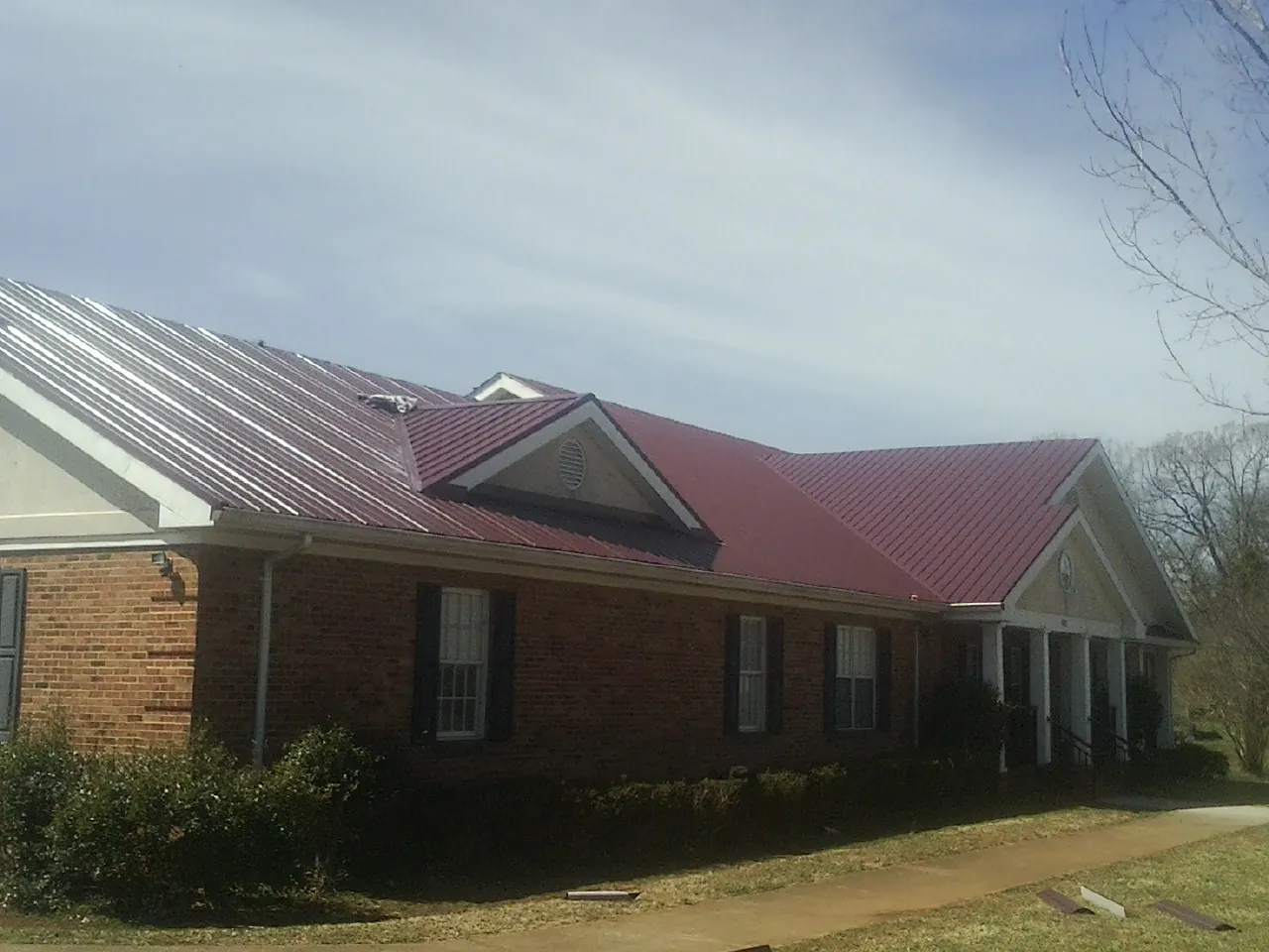 Red metal roof with gabled entries on a long brick building, from a Hail Damage Roof Repair job in Boylston