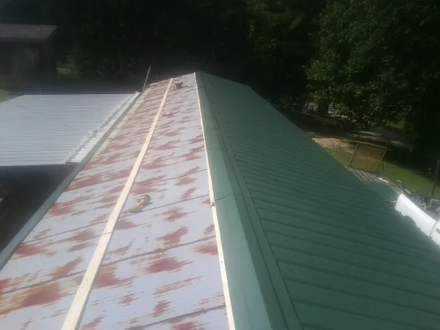 Old rusted panels beside newly installed green metal roofing — Wind Damage Roof Repair by Roofing Brothers in Boylston