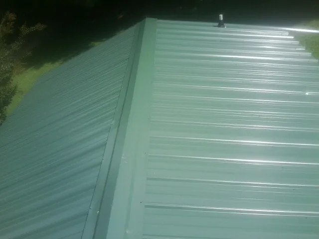 New green metal panels meeting at the ridge of a roof — Flat Roof Repair work by our crew in Boylston
