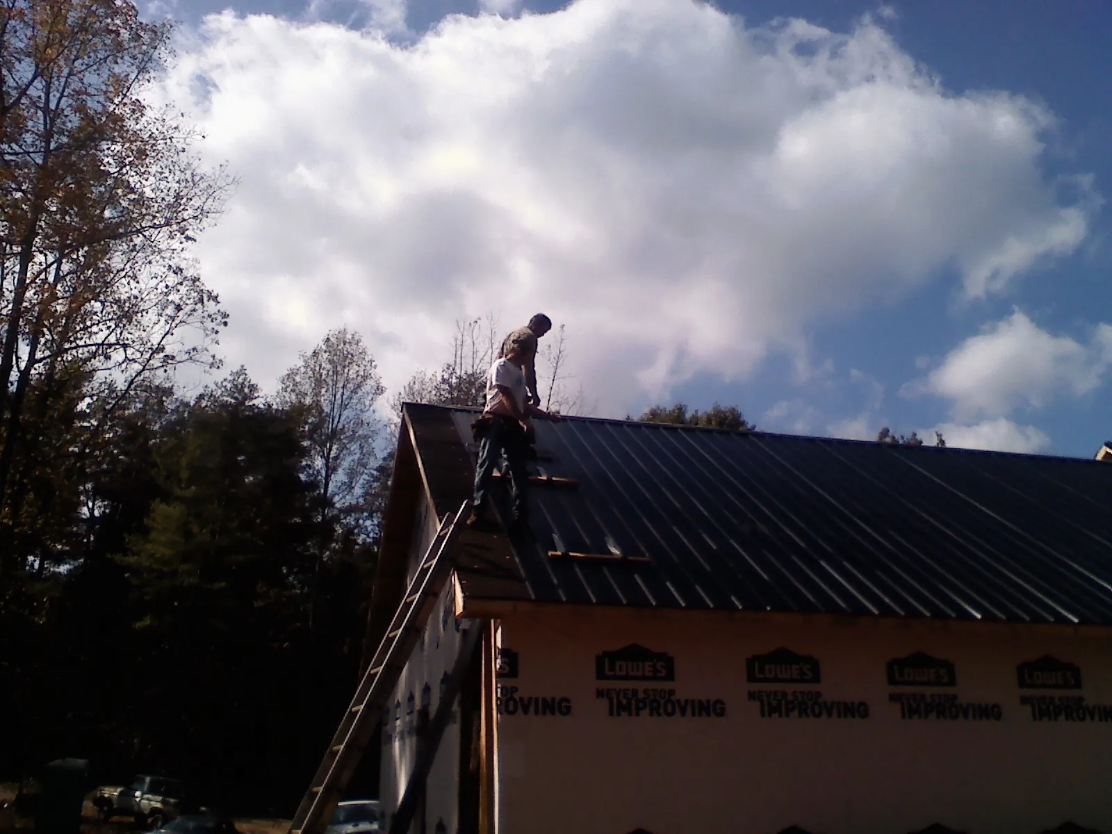 Roofer fastening dark metal panels high against a cloudy sky, from a Roof Inspection job in Boylston