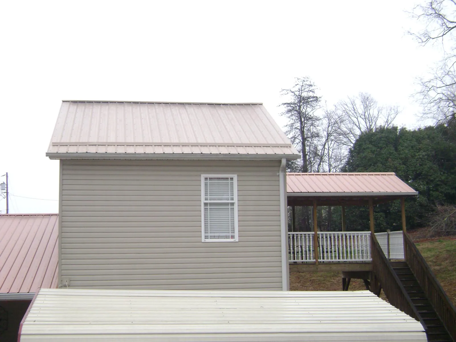 Tan metal roofs on a two story addition and attached porch, from a Roof Replacement job in Boylston